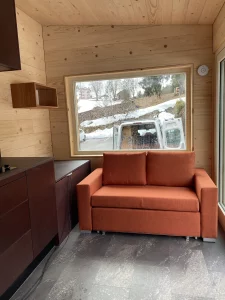 Salon de la tiny house avec canapé et grandes fenêtres réalisé par Solutions Bois